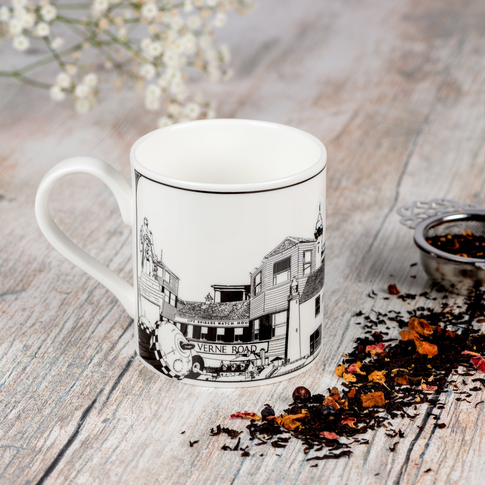 Fine china mug featuring landmarks from Tynemouth, Cullercoats, Whitley Bay and North Shields. With a silver tea strainer and scattered tea leaves.