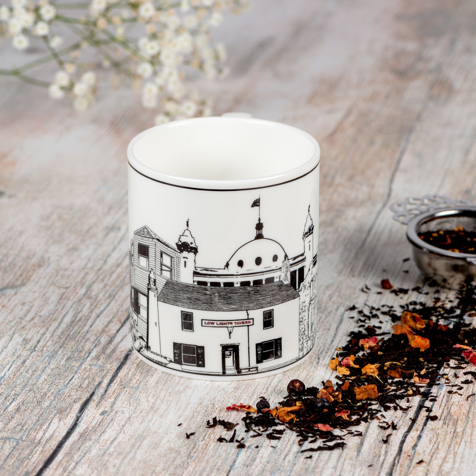 Fine china mug featuring landmarks from Tynemouth, Cullercoats, Whitley Bay and North Shields. With a silver tea strainer and scattered tea leaves.