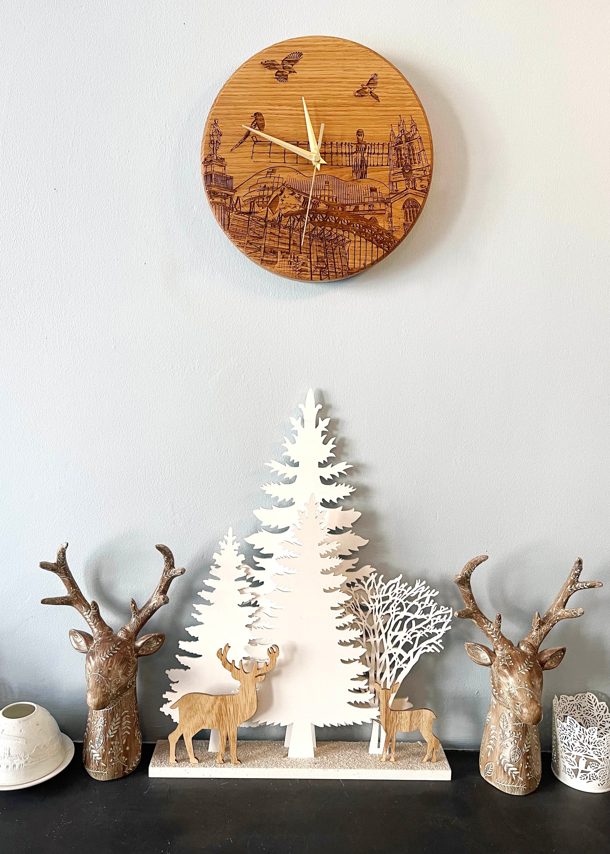 Laser engraved solid oak clock on mantle piece with stag ornaments. Engraving on the clock features landmarks such as St James' Park, Greys Monument, The Glasshouse, Newcastle Cathedral, The Tyne Bridge, Angel of the North and Newcastle Cathedral. 